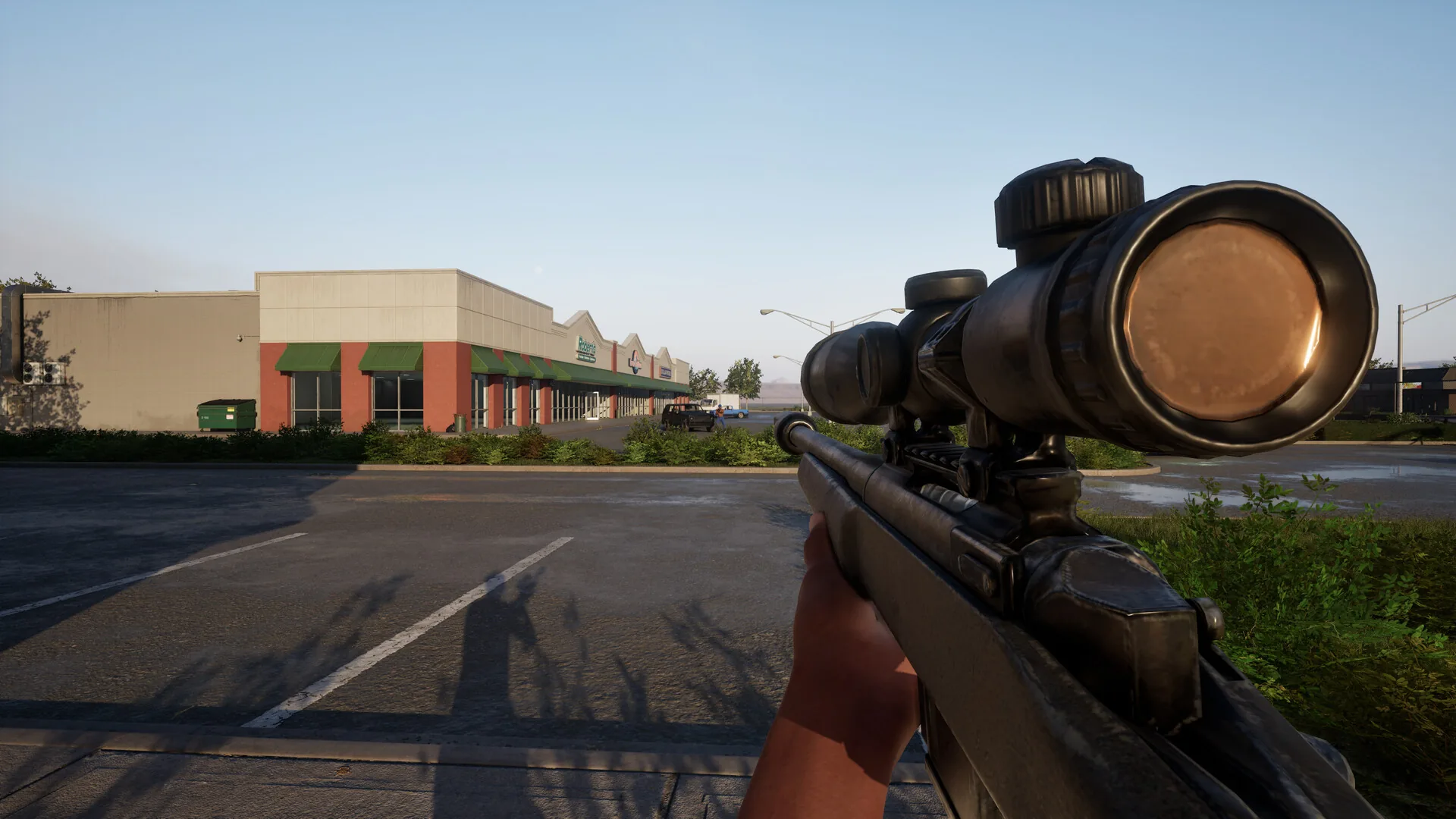 First-person view of a firearm fitted with a large scope beside a parking lot.